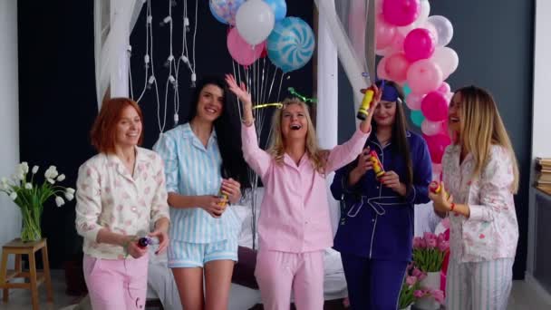 Группа девушек, смеющихся и улыбающихся в пижаме, запускает конфетти в замедленной съемке 120 кадров в секунду. Подушки безопасности, блестящие конфеты на вечеринке — стоковое видео