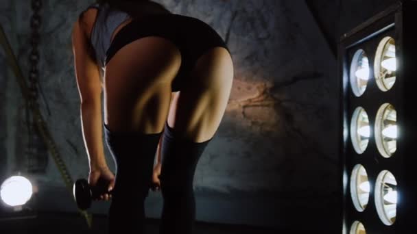 Λεπτή σέξι αθλητής εκτελεί πλαγιές κάτω με αλτήρες σε κοντό σορτς. Ασκήσεις για να ενισχύσει τους μυς των ισχίων. Λεπτή σέξι αθλητής εκτελεί πλαγιές κάτω με αλτήρες. Γενικό σχέδιο του — Αρχείο Βίντεο