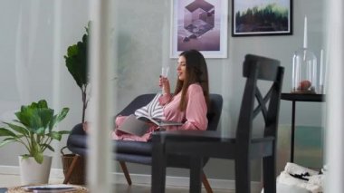 Güzel bir kız seksi pembe pijama parlak kanepede yatan ve cam şampanya içmek dergi okur.