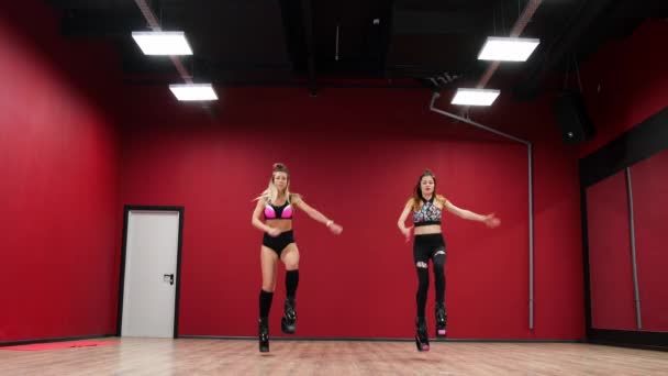 两个漂亮的体育女孩做一个活跃的脂肪燃烧锻炼像袋鼠在特殊的健身鞋跳。锻炼耐力。kango 跳跃 — 图库视频影像