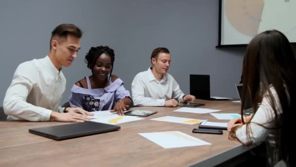 Un grupo de gerentes multiétnicos creativos desmontan en la reunión del consejo de administración en la sala de conferencias los gráficos de ganancias del último año en la firma. El jefe de un africano — Vídeo de stock