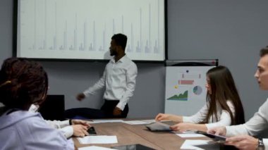 Afrika kökenli Amerikalı antrenör ofiste iş adamları için kurumsal tanıtım sağlar, koyu tenli işadamı yeni iş planı üzerinde beyaz tahta, istemcilere toplantısında hoparlör dinleme konuşma sunar