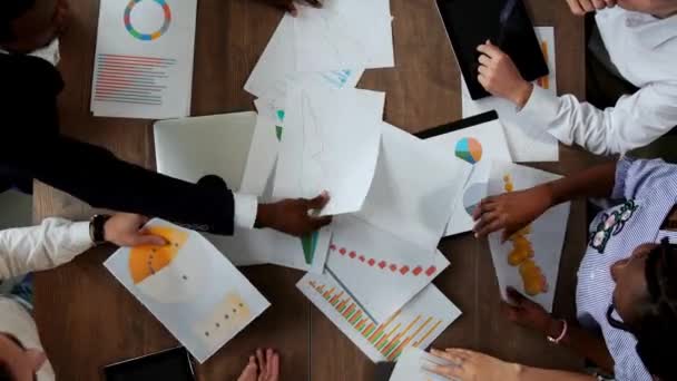 Bovenaanzicht van het grote bureau waarachter het office-team van creatieve managers van verschillende nationaliteiten brainstormen maakt. Bespreking van de problemen op de beurs. De opkomst en ondergang van de — Stockvideo