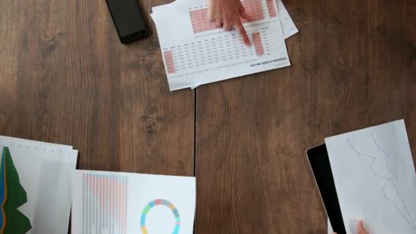 Bovenaanzicht van het grote bureau waarachter het office-team van creatieve managers van verschillende nationaliteiten brainstormen maakt. Close-up camera beweegt langs de tafel, verspreiding van de documenten van financiële — Stockvideo