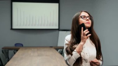 Office elbiseleri zamanlamaları çerçevede ofiste bir cep telefonu konuşurken gözlüklü bir konferans odasında duran güzel bir kız portresi