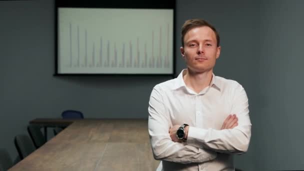 Retrato de um homem com uma camisa branca em pé no escritório no fundo da mesa de conferência, e a imagem do gráfico no projetor — Vídeo de Stock