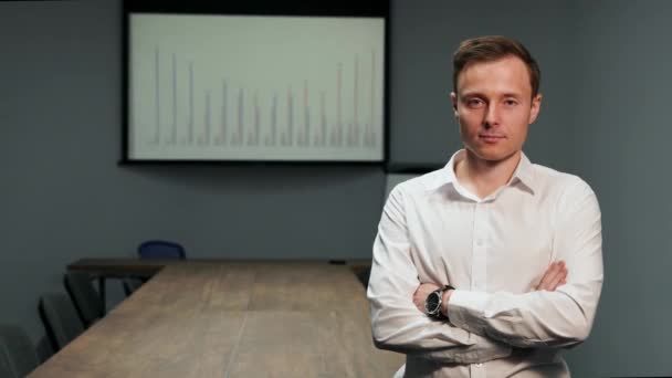 Retrato de um homem com uma camisa branca em pé no escritório no fundo da mesa de conferência, e a imagem do gráfico no projetor — Vídeo de Stock