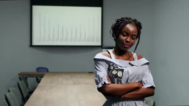 Retrato de una mujer de negocios afroamericana de pie en el cargo frente a una gran mesa y gráficos en la pantalla mirando a la cámara — Vídeos de Stock