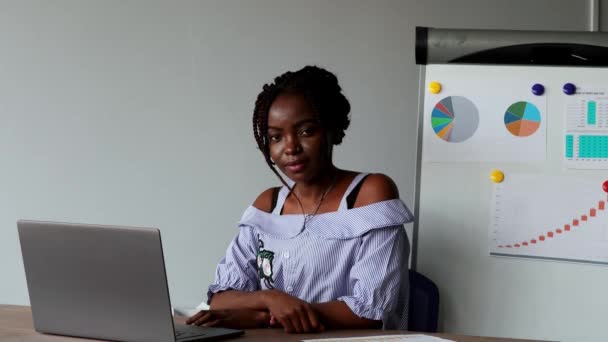 Bir Afro Amerikan portresi office office giysileri içinde laptop, grafikler ve tablolar arka plan üzerinde oturan güzel kız. Kameraya bakarak — Stok video