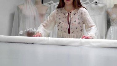 Giysi Tasarımcısı studio tablo üzerinde ölçümler ile çalışıyor. 4 k Uhd vurdu. Tatlı beyaz ve açık renkli dikiş yavaş beyaz kumaş skein dağıtın. el yapımı terzilik