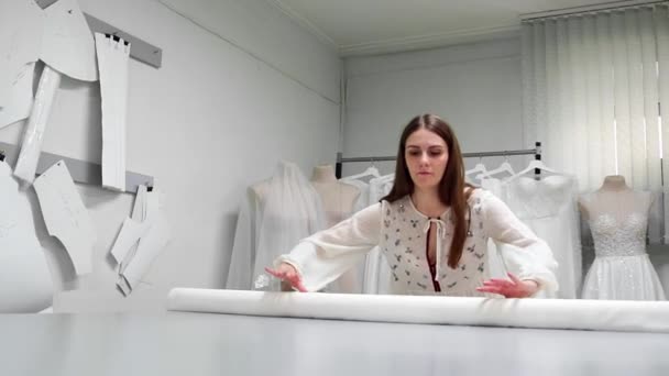 Giysi Tasarımcısı studio tablo üzerinde ölçümler ile çalışıyor. 4 k Uhd vurdu. Tatlı beyaz ve açık renkli dikiş yavaş beyaz kumaş skein dağıtın. el yapımı terzilik — Stok video