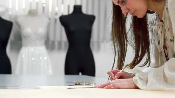 Hermosa chica diseñadora de moda se basa en las plantillas de papel para cortar la tela en los maniquíes vestidos con vestidos de novia. Fabricante de vestidos de novia . — Vídeos de Stock