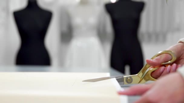 Красивая модельер девушка вырезать на бумаге с золотыми ножницами узоры для ткани на фоне манекенов одеты в свадебные платья. Производитель свадебных платьев . — стоковое видео