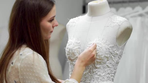 Портрет дівчини, що створює весільну сукню за ексклюзивним замовленням, пошиває тканини та стрази на одязі, одягненому в манекен. виробництво весільних суконь. Маленький бізнес — стокове відео