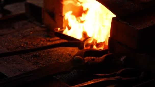 Close-up van een smid wakkeren de vlammen van de oven, met behulp van de tools voorkomt sintels, vonken vliegen naar de kant in slow motion. Close-up van smeden hand. — Stockvideo