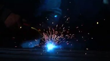 Kaynakçı bir maske yavaş çalışır. Farklı yönlere kıvılcımlar. Kaynak mavi renk kızdırma. Çelik malzeme ile çalışmak