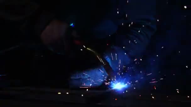 The welder works in a mask in slow motion. Sparks fly in different directions. Blue color glow welding. Work with steel materials — Stock Video