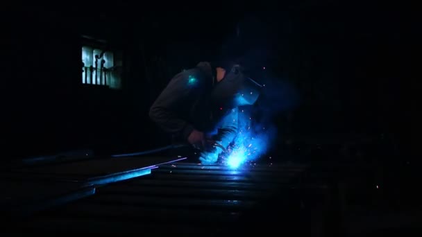 The welder works in a mask in slow motion. Sparks fly in different directions. Blue color glow welding. Work with steel materials — Stock Video