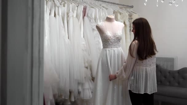 Gyönyörű lány esküvői ruha keresi az utastérben, összehasonlítva más ruhák. Készül az esküvőre. Vásárol egy esküvői ruha. A varrónő ellenőrzi a kész rendelésre készült esküvői ruha. — Stock videók