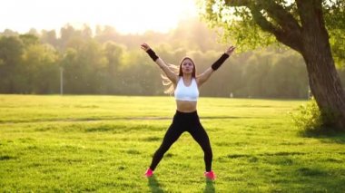 Sportif esmer bir beyaz top kasları siyah dar pantolon ve pembe spor ayakkabı içinde güneş ışığı uzanıyor ve eğitim alanında orman arka planı temiz havada hazırlar.