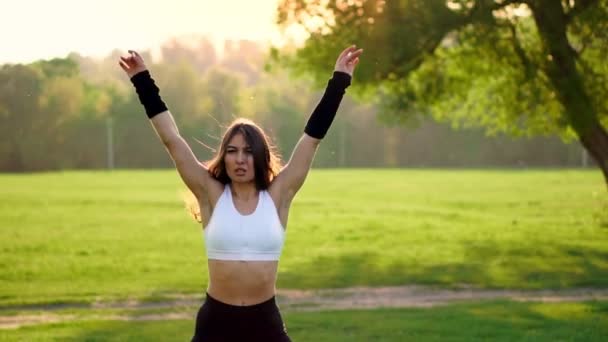 Female fitness instructor doing jumping jacks exercising in green park — Stock Video