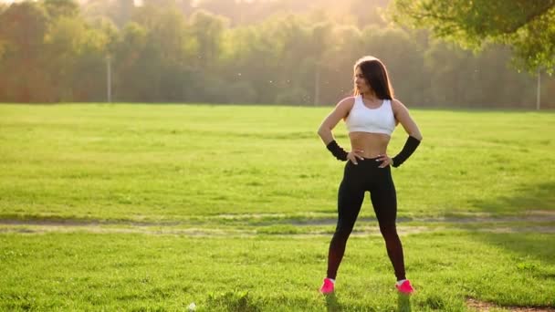 Mooie jongedame luisteren muziek in het park tijdens het hardlopen. Portret van lachende sportieve meisje met oortelefoon kijken camera op park in het najaar. Vrouw atleet camera kijken tijdens zonsondergang in de winter. — Stockvideo