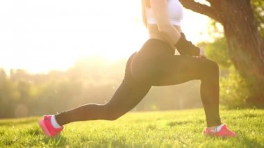 İnce atletik kadın diz-bounce egzersiz veya lunges yapıyor Park'ta çalışma dışarı. Çim pembe spor ayakkabı günbatımı ayak yakın çekim