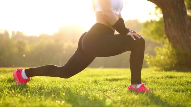 İnce atletik kadın diz-bounce egzersiz veya lunges yapıyor Park'ta çalışma dışarı. Çim pembe spor ayakkabı günbatımı ayak yakın çekim — Stok video