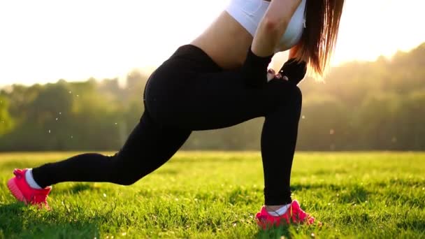 Femme athlétique mince travaillant dans le parc faisant de l'exercice de rebond du genou ou se jette. Coucher de soleil pieds fermer en baskets roses sur l'herbe — Video