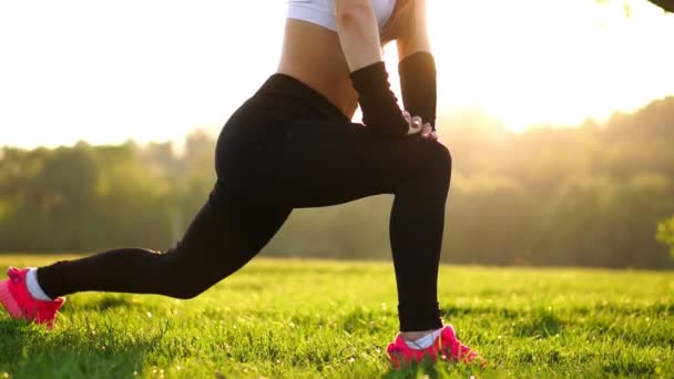 Schlanke, athletische Frau, die im Park mit Knie-Sprungübungen oder Ausfallübungen trainiert. Füße bei Sonnenuntergang hautnah in rosa Turnschuhen im Gras — Stockvideo