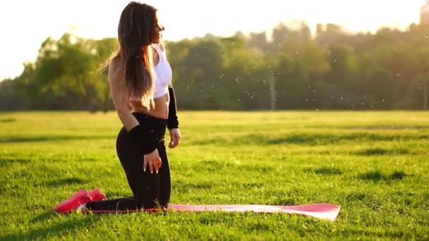Ung och vacker kvinna sitter på mattan under paus i sin fitness träning. Vila efter träning i solljuset korrigera håret i slow motion. Hår i bakgrundsbelysningen. — Stockvideo