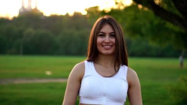 Genç güzel kadın Park çalışırken müzik dinleme. Sonbaharda park kameraya bakarak kulaklık ile gülümseyen sportif kız portresi. Kadın atlet Kış günbatımı sırasında kameraya bakıyor.