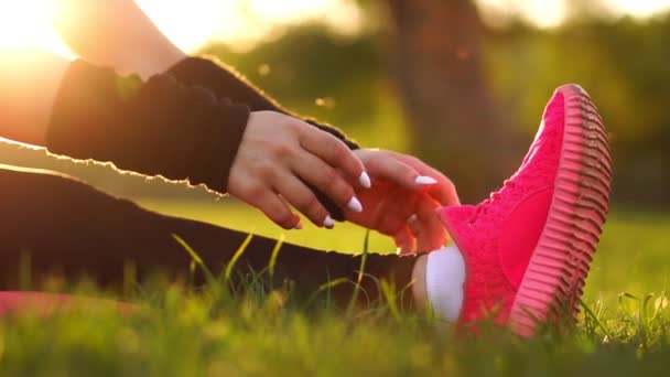 Närbild händer ta över enda av gymnastikskor på gräset i solljus. Uppvärmning inför morgonjogg. Vacker brunett på en körning i parken. — Stockvideo