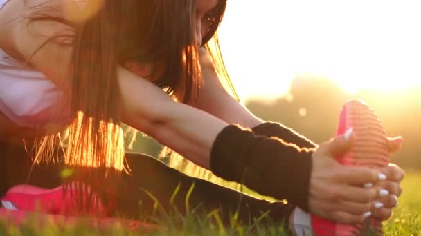 Närbild händer ta över enda av gymnastikskor på gräset i solljus. Uppvärmning inför morgonjogg. Vacker brunett på en körning i parken. — Stockvideo