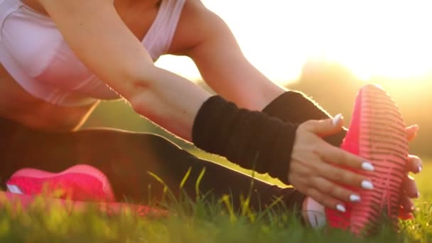 Närbild händer ta över enda av gymnastikskor på gräset i solljus. Uppvärmning inför morgonjogg. Vacker brunett på en körning i parken. — Stockvideo