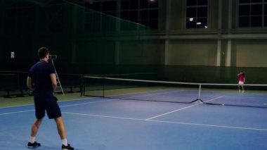 Profesyonel tenis oyuncusu tarafından hizmet. Tenis tenis salonu kapalı hizmet. Adam hizmet tenis raket ve giymiş siyah gömlek, siyah şort ve siyah ayakkabı.