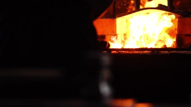 Primer plano de un martillo herrero sobre el fondo de llamas ardientes del horno . — Vídeo de stock