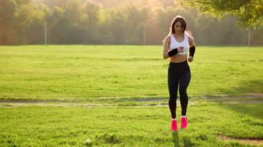 Beyaz bir üst ve pembe ayakkabı çimenlerde sportif kız bir alanda gün batımında ısınma kalça kaldırma önce çalışma yapar. Spor. yakın çekim. Çimen spor ayakkabı