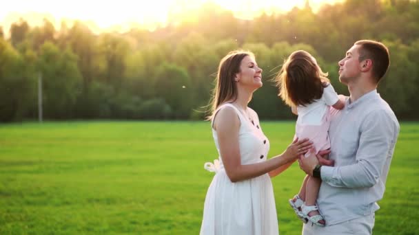 Gelukkig jonge gezin met kind lopen op zomer veld. Gezonde moeder, vader en dochter meisje genieten van natuur, samen, buiten. Zonsondergang. — Stockvideo
