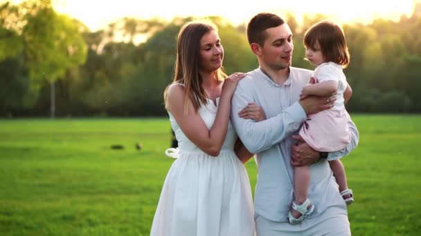 Familia joven feliz con niño caminando en el campo de verano. Madre sana, padre e hija pequeña disfrutando de la naturaleza juntos, al aire libre. Puesta de sol . — Vídeo de stock