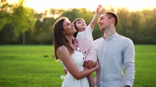 Familia joven feliz con niño caminando en el campo de verano. Madre sana, padre e hija pequeña disfrutando de la naturaleza juntos, al aire libre. Puesta de sol . — Vídeos de Stock