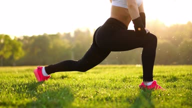 Sportif esmer bir beyaz top kasları siyah dar pantolon ve pembe spor ayakkabı içinde güneş ışığı uzanıyor ve eğitim alanında orman arka planı temiz havada hazırlar.