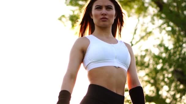 Jovem mulher bonita ouvir música no parque enquanto corre. Retrato de menina desportiva sorridente com fone de ouvido olhando para a câmera no parque no outono. Mulher atleta olhando para a câmera durante o pôr do sol de inverno . — Vídeo de Stock