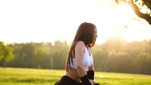 Szczupła kobieta lekkoatletycznego w parku robi ćwiczenia kolana bounce lub rzuca. Zachód słońca stóp z bliska w różowe trampki na trawie — Wideo stockowe