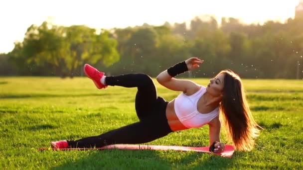 Mulher fazendo crunches abdominais exercício no tapete de fitness no parque de verão Em câmera lenta ao pôr do sol . — Vídeo de Stock