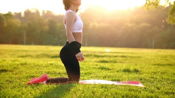 Молодая и красивая женщина сидит на коврике во время перерыва в ее фитнес-тренировки. Отдых после физических упражнений в солнечном свете коррекции волос в замедленной съемке. Волосы в подсветке . — стоковое видео