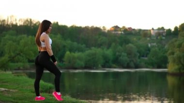 Genç ve güzel bir kadın onun fitness egzersiz tatilinde mindere oturuyor. Ağır çekimde saç düzeltme güneş ışığı altında egzersiz sonrası dinlenme. Arka ışık saç.