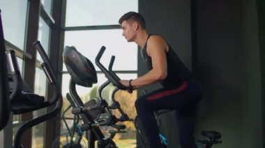 Spor salonundaki sportif formda genç bir adam eliptik antrenör üzerinde egzersiz yapıyor. Zor.