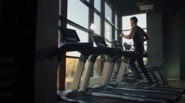 Spor salonunda spor yapan ve koşu bandında koşan genç erkek ve kadınlar. Büyük bir panoramik pencerenin yanında