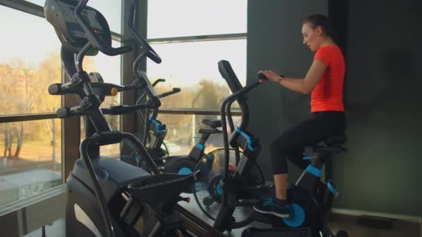 활달 한 젊은 여성 이 트레이너와 함께 체육관에서 에어 자전거를 돌립니다. 비행기를 타고 훈련하는 암컷. — 비디오
